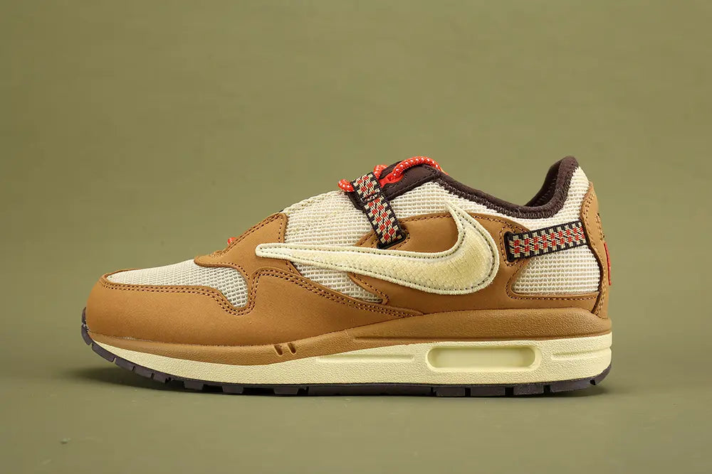 Air Max 1 Cactus Jack Wheat Lemon Drop DO9392-701 - Heel Counter Close Up on Olive Background Showing Red Triangular Pennant Flag Badge with White Swoosh Logo Diamond-Pattern Woven Ribbon Pull Tab Dark Brown Baroque Brown Suede Ankle Collar and Red Textile Collar Lining