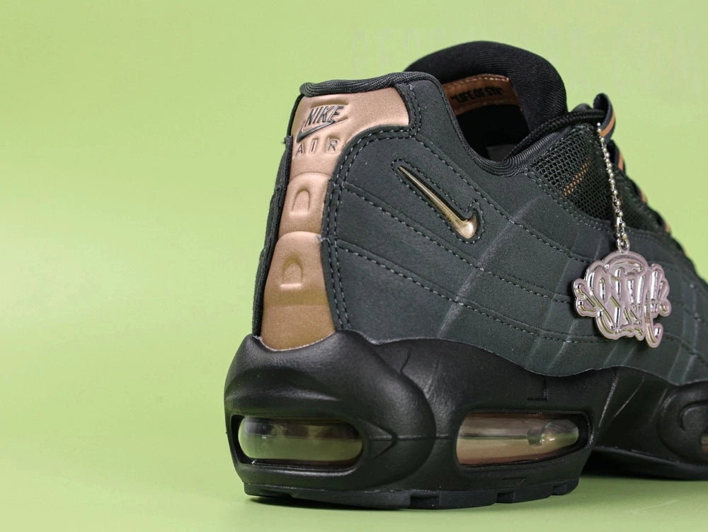 Central Cee x Air Max 95 Black and Gold - Tongue Close Up Showing Embroidered Oval Air Max Badge in Copper and Grey on Black on Green Background