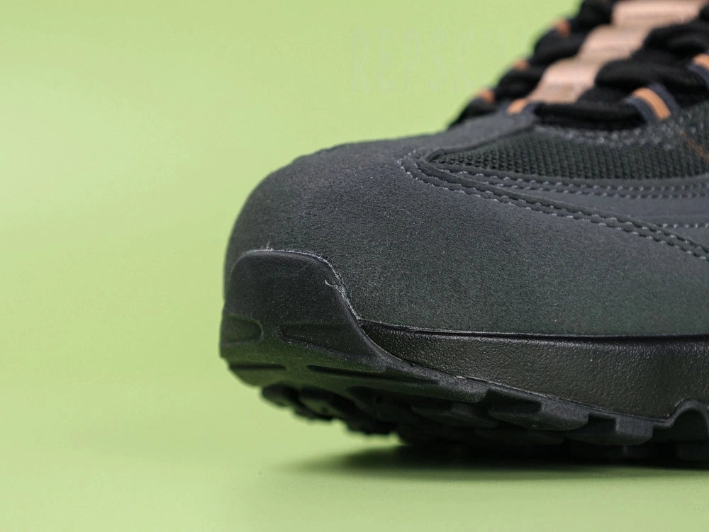 Central Cee x Air Max 95 Black and Gold - Quarter Panel Close Up Showing 3D Sculpted Bronze Metallic Recessed Swoosh on Anthracite Nubuck on Green Background