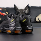Corteiz x Air Max 95 SP Honey Blacks - Tongue Close Up Showing Oval Corteiz Alcatraz Badge in Gold on Black and Gold Nike Air Text on Dark Background
