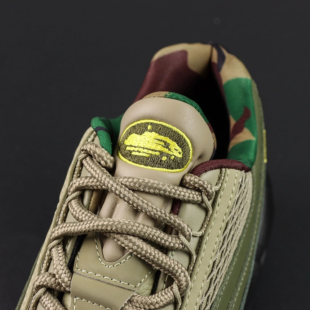 Corteiz x Air Max 95 SP Gutta Green - Toe Box Close Up Showing Volt CRTZ Monogram Logo Embroidery on Dark Olive Leather and Khaki Diamond Quilted Mesh Panel on Dark Background