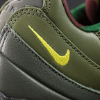 Corteiz x Air Max 95 SP Gutta Green - Quarter Panel Close Up Showing Volt Embroidered Mini Swoosh on Dark Olive Leather and Burgundy Collar Lining on Dark Background