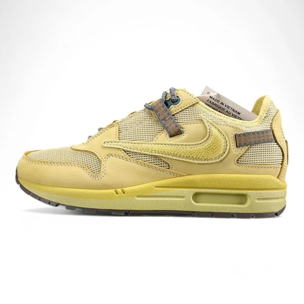 Air Max 1 Cactus Jack Saturn Gold Tea Tree Mist - Full Lateral Profile View on Olive Background Showing Saturn Gold Woven-Texture Swoosh Cream Coarse Square-Grid Woven Mesh Toe Box and Lateral Midfoot Saturn Gold Nubuck Overlays Multicolour Reflective Woven Webbing Lace Loops Teal Circular Lace Lock Grey Rope Laces Saturn Gold Suede Mudguard and Saturn Gold AM1 Midsole with Heel Air Window