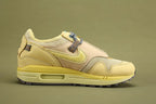 Air Max 1 Cactus Jack Saturn Gold Tea Tree Mist - Toe Box Close Up on Olive Background Showing Cream Coarse Square-Grid Woven Mesh Toe Box Body Saturn Gold Smooth Nubuck Toe Box Overlay with Yellow Tonal Edge Stitching Multicolour Reflective Woven Webbing Lace Loops Grey Rope Laces with Multicolour Speckle and Saturn Gold AM1 Midsole with Saturn Gold Suede Mudguard and Dark Grey Rubber Outsole