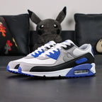 Air Max 90 Hyper Royal 2020 - Lateral Side View with Pikachu on Sofa Showing Full Upper Construction Grey Suede Swoosh Hyper Royal Blue Rear Panel and Air Max Blue Midsole Text