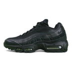 Air Max 95 Essential Triple Black - Lateral Side View on Green Background Showing Full Tonal Black Upper Black Leather Toe Box Black Mesh Quarter Panel and Tonal Black Spine Overlays