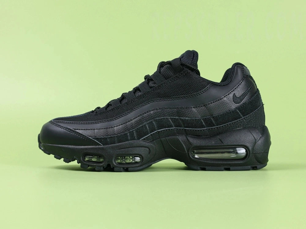 Air Max 95 Essential Triple Black - Pair Heel Rear View on Green Background Showing Black Snake Embossed Leather Heel Counter with Tonal Black Swoosh and Air Text