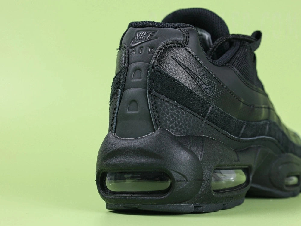Air Max 95 Essential Triple Black - Tongue Close Up on Green Background Showing Grey Embroidered Oval Airmax Badge on Black Tongue