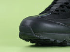 Air Max 95 Essential Triple Black - Heel Lateral Close Up on Green Background Showing Black Snake Embossed Leather Panel with Tonal Black Embroidered Swoosh and Black Mesh Quarter Panel Detail