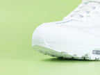 Air Max 95 Essential White Grey Fog - Heel Rear Angled View on Green Background Showing Full White Leather Heel Counter Tonal White Panel and Translucent Clear Heel Air Unit