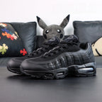 Air Max 95 OG Black Anthracite 2025 - Pair Three Quarter Lateral View with Red Shoebox on Sofa Showing Full Tonal Black Upper Black to Anthracite Gradient Spine and Smoke Blue Air Units