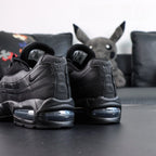 Air Max 95 OG Black Anthracite 2025 - Pair Heel Rear View with Pikachu on Sofa Showing Tonal Black Anthracite Heel Badge Air Text and Swoosh on Both Shoes with Smoke Blue Air Units