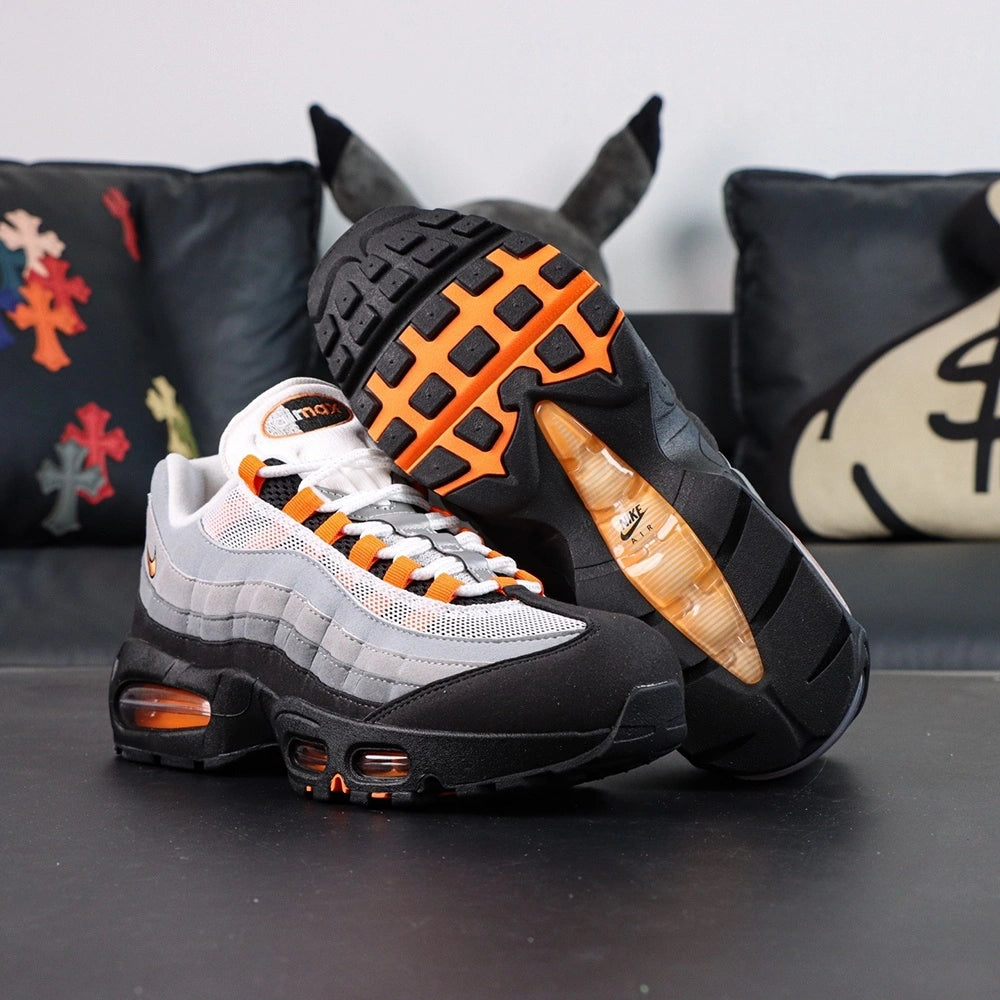 Air Max 95 OG Bright Mandarin 2.0 2025 - Pair Three Quarter Lateral View with Red Shoebox on Sofa Showing Full Upper Construction Black Suede Toe Box Grey Gradient Spine Orange Swoosh Orange Lace Loops and Orange Air Units