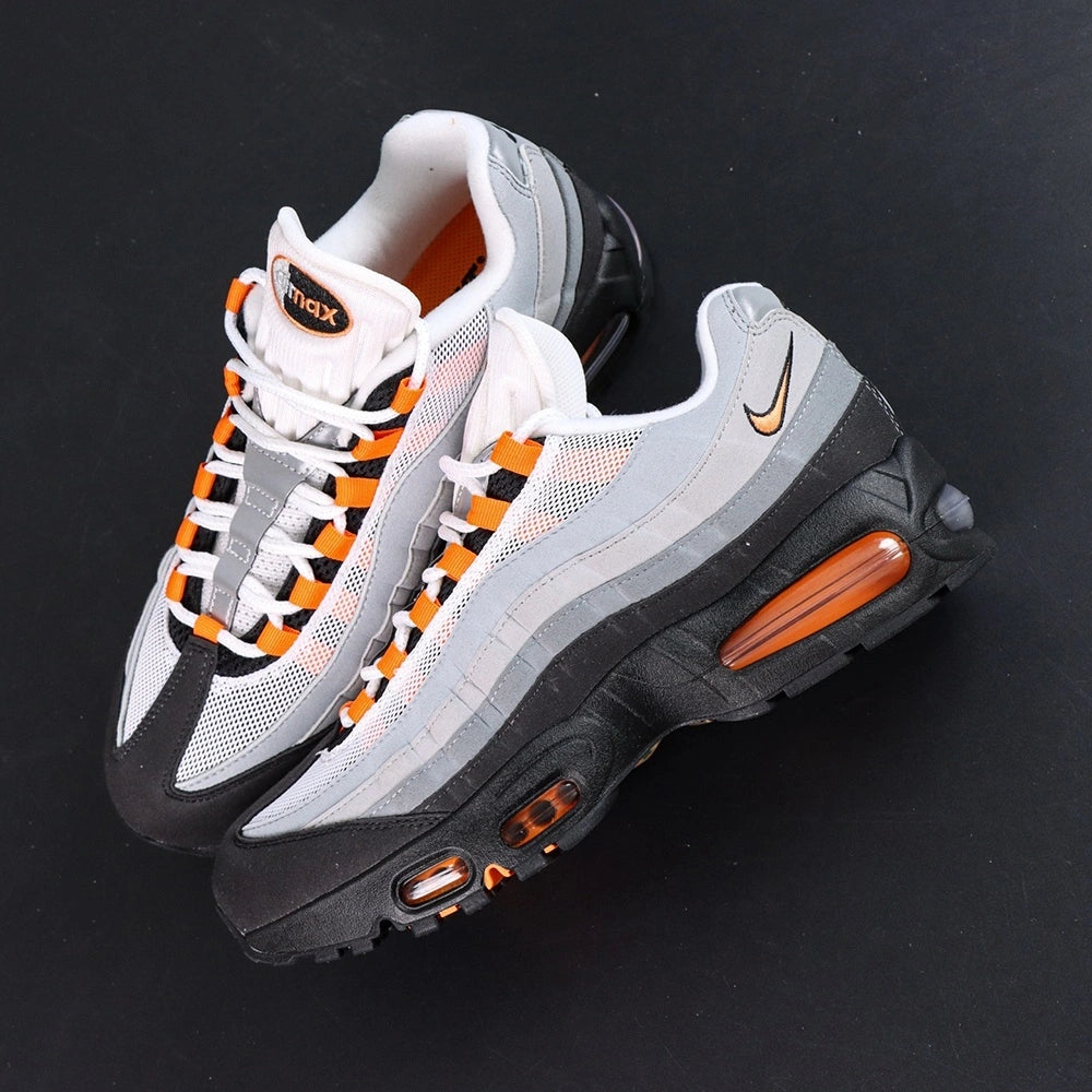 Air Max 95 OG Bright Mandarin 2.0 2025 - Pair Three Quarter Lateral View with Pikachu on Sofa Showing Full Upper Black Suede Toe Box Grey Gradient Spine Orange Mini Swoosh Orange Lace Loops and Orange Air Units