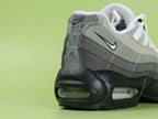 Air Max 95 OG Grey Gradient - Lateral Spine Swoosh Close Up on Green Background Showing White and Black Dual Tone Embroidered Mini Swoosh on Medium Grey Suede Spine Panel with Dark Charcoal Lower Spine