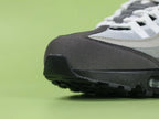 Air Max 95 OG Grey Gradient - Heel Rear Angled View on Green Background Showing Grey Suede Heel Badge with Black Nike Air Text Tonal Grey Swoosh and Translucent Smoke Heel Air Unit in Black Midsole