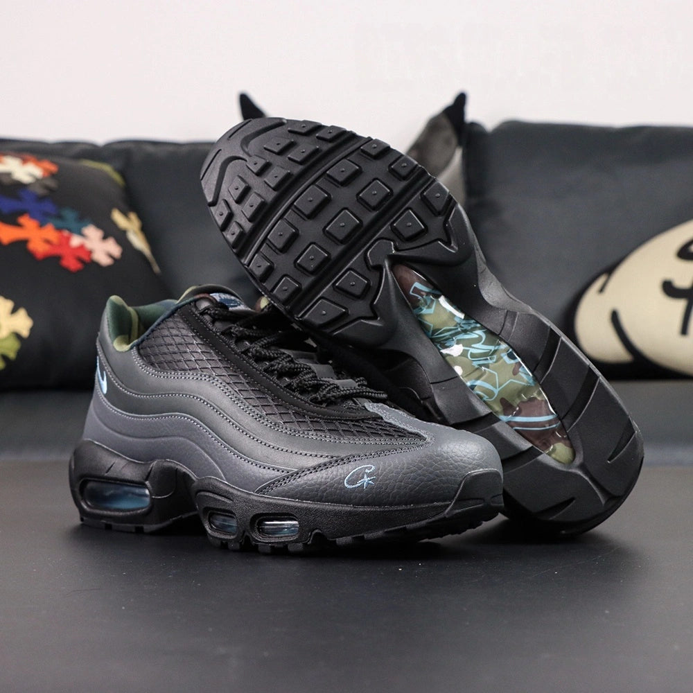 Air Max 95 SP Corteiz Aegean Storm - Pair Three Quarter Lateral Top Down View on Dark Background Showing Full Black Upper Diamond Quilted Mesh Black Charcoal Gradient Spine Iridescent Blue Swoosh White Corteiz Script Embroidery and Camo Collar Lining