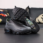 Air Max 95 SP Corteiz Aegean Storm - Pair Three Quarter Lateral Top Down View on Dark Background Showing Full Black Upper Diamond Quilted Mesh Black Charcoal Gradient Spine Iridescent Blue Swoosh White Corteiz Script Embroidery and Camo Collar Lining
