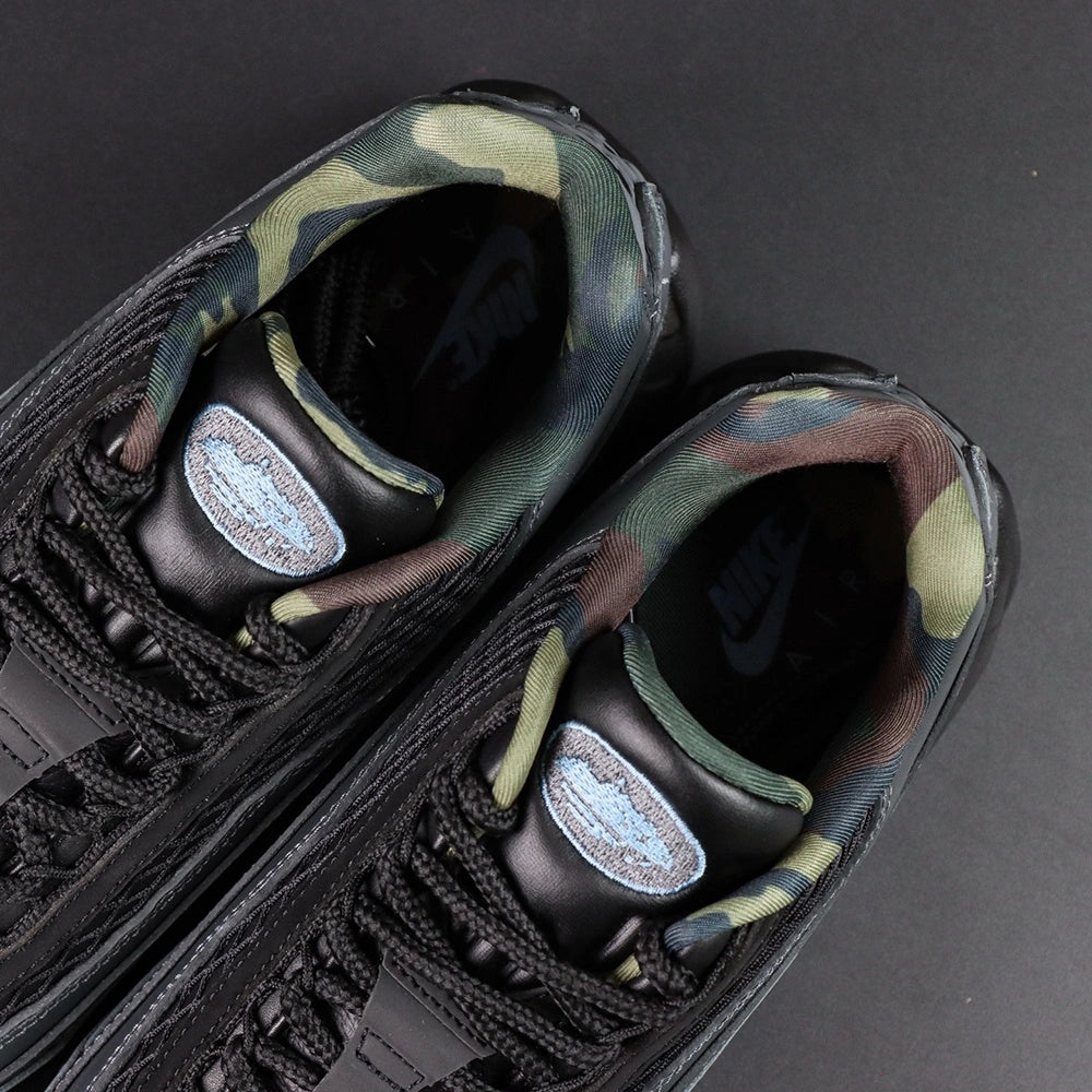 Air Max 95 SP Corteiz Aegean Storm - Pair Three Quarter Lateral View with Orange Shoebox on Sofa Showing Full Black Upper Diamond Quilted Mesh Black Charcoal Gradient Spine White Corteiz Script on Toe Box and Steel Blue Air Units