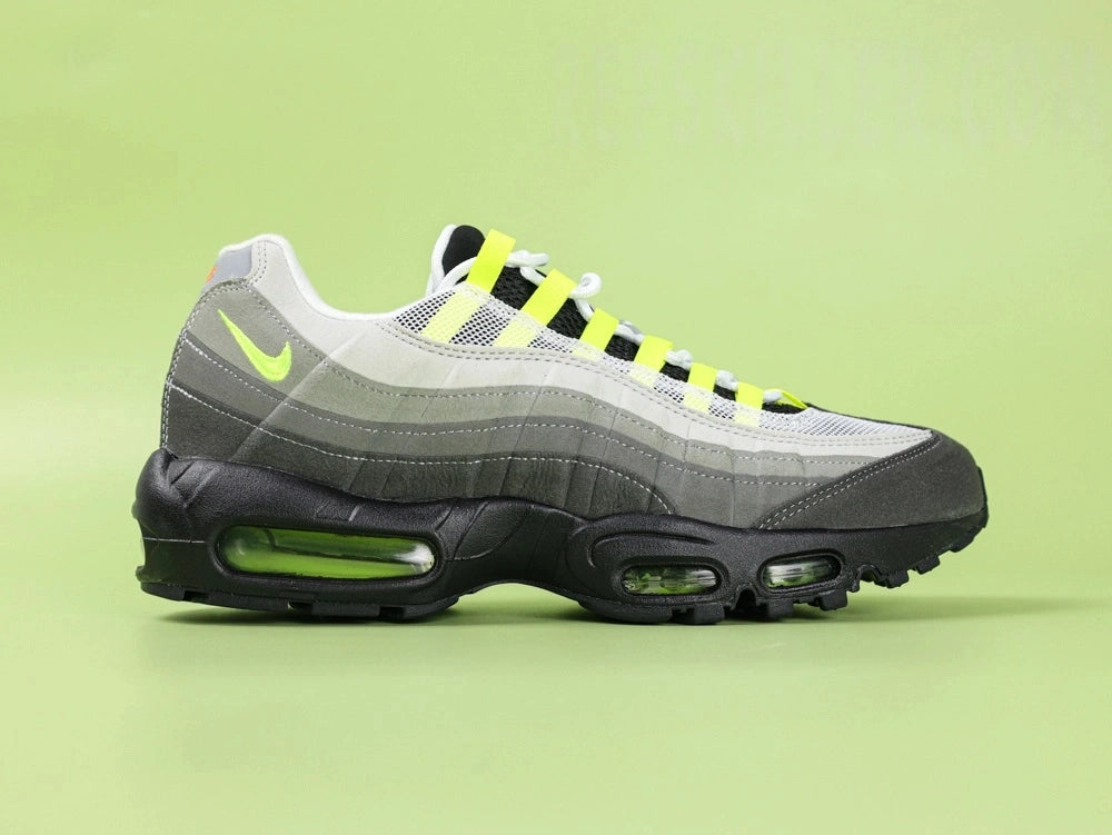Air Max 95 TT Greedy - Heel Rear Angled View on Green Background Showing Grey Suede Heel Badge with Orange Nike Air Text Volt Neon Lace Loops and Volt Translucent Heel Air Unit in Black Midsole
