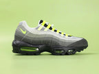 Air Max 95 TT Greedy - Heel Rear Angled View on Green Background Showing Grey Suede Heel Badge with Orange Nike Air Text Volt Neon Lace Loops and Volt Translucent Heel Air Unit in Black Midsole