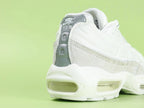Air Max 95 x Comme des Garçons White - Tongue Close Up on Green Background Showing White Ribbed Fabric Tongue with Tonal White Embroidered Oval Airmax Badge