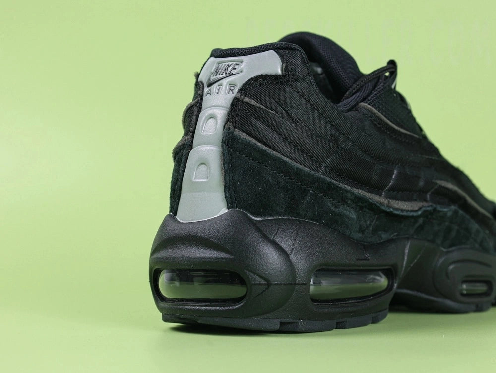 Air Max 95 x Comme des Garçons Black - Tongue Close Up on Green Background Showing Black Ribbed Fabric Tongue with Tonal Black Embroidered Oval Airmax Badge
