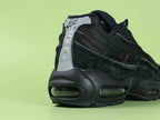 Air Max 95 x Comme des Garçons Black - Tongue Close Up on Green Background Showing Black Ribbed Fabric Tongue with Tonal Black Embroidered Oval Airmax Badge