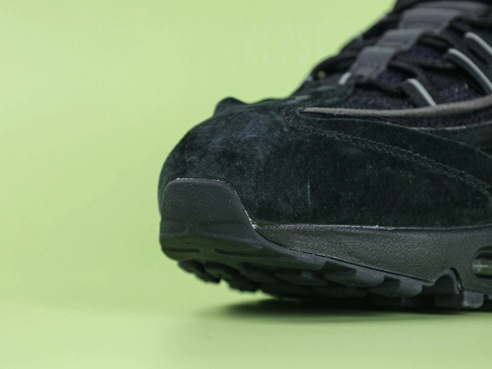 Air Max 95 x Comme des Garçons Black - Heel Angled View on Green Background Showing Silver AM95 Heel Stabiliser AIR Text Black Rope Laces and Black Translucent Heel Air Unit