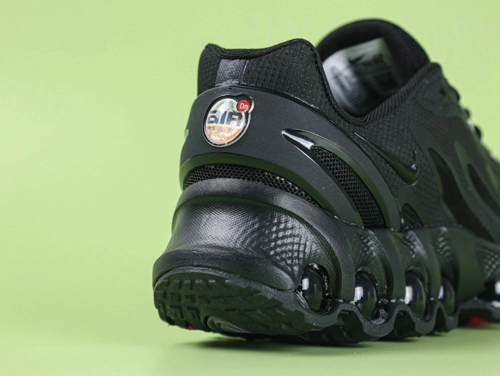 Air Max Dn8 All Black - Tongue Close Up on Green Background Showing Tonal Black Rubber Oval AIRMAX Badge Debossed on Black Mesh Tongue