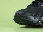 Air Max Dn8 All Black - Lateral Swoosh Close Up on Green Background Showing High-Gloss Lacquered Black Swoosh on Black Engineered Mesh Midfoot with Flame-Shaped TPU Cut-Out Overlays