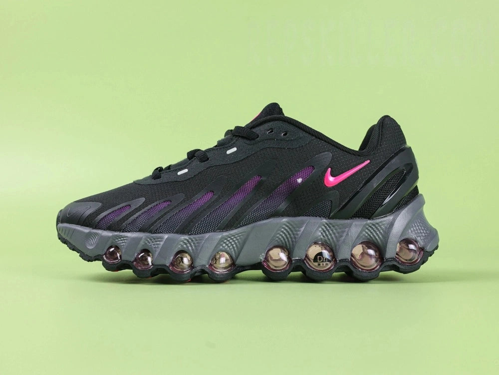 Air Max Dn8 Black Purple - Outsole View on Green Background Showing Full Black Rubber Outsole with Vivid Fuchsia Magenta Air Cushion Window Red Circular Traction Studs and Gold Circular Dn Badge at Midfoot