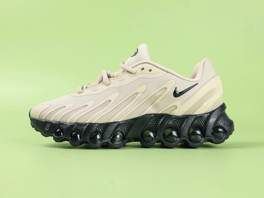 Air Max Dn8 Desert Khaki Black - Outsole View on Green Background Showing Full Black Rubber Outsole with Large Blue Air Cushion Windows at Forefoot and Heel Red Circular Traction Studs and Gold Circular Dn Badge at Midfoot