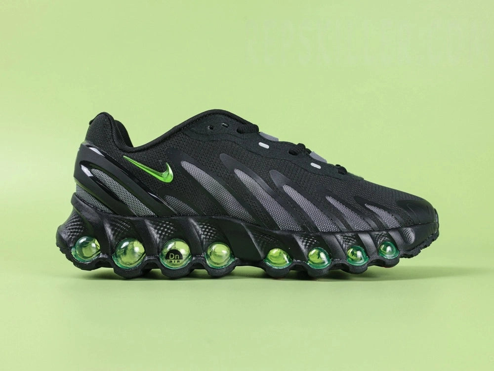 Air Max Dn8 Black Volt - Tongue Close Up on Green Background Showing Grey Oval AIRMAX Badge with Volt Green Lettering and Orange Circular Dn8 Insole Badge