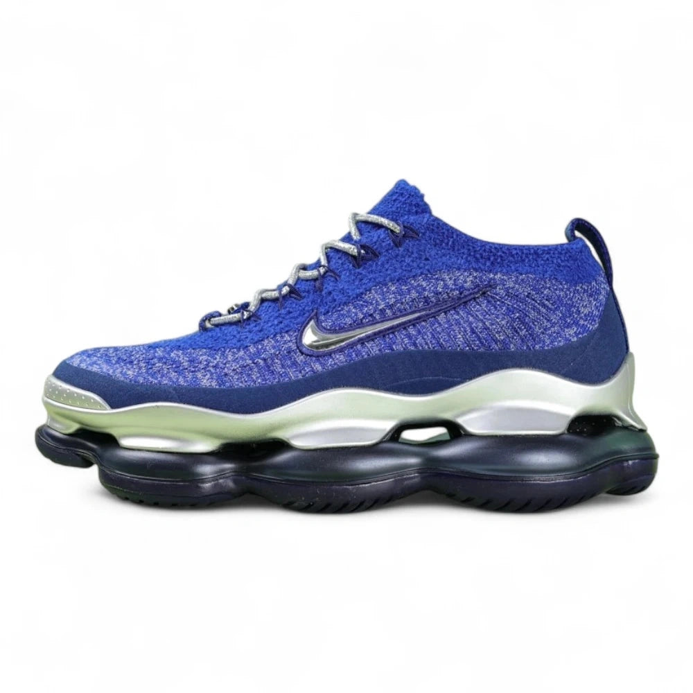Air Max Scorpion FK Blue Fury - Full Lateral Profile View on Green Background Showing Royal Blue Navy Flyknit Upper Silver Metallic Midsole Shell and Deep Navy Blue Scorpion Air Pod Outsole
