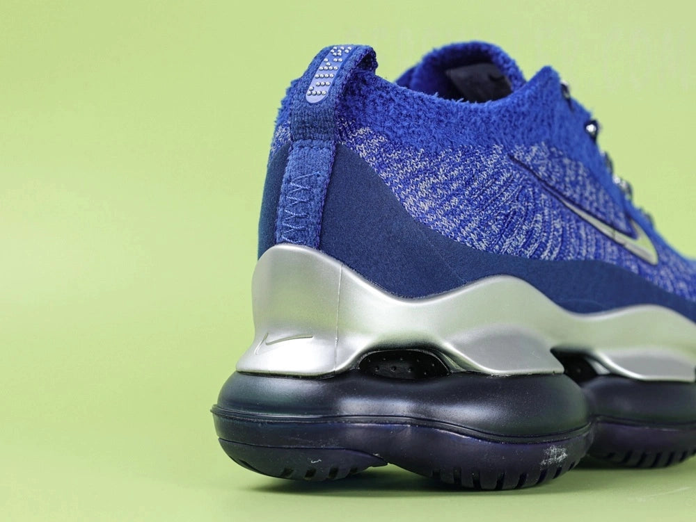 Air Max Scorpion FK Blue Fury - Tongue Lace Area Close Up on Green Background Showing Two Blue Rubber Lace Keeper Tabs with Silver Raised Dot Matrix Pattern and Silver Metallic Rope Laces