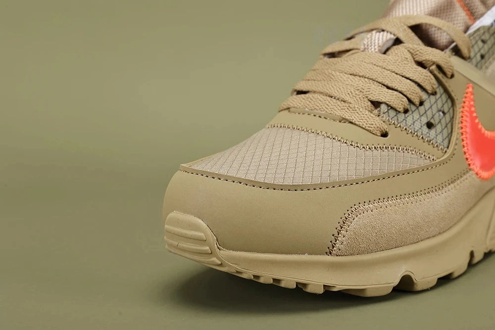 Off-White x Air Max 90 Desert Ore - Tongue and Lace Area Close Up on Olive Background Showing White Woven NIKE SPORTSWEAR Label with Orange Swoosh Metallic Gold Shimmer Tongue Lining and Hot Coral Overlock Stitching on Suede Overlays