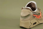 Off-White x Air Max 90 Desert Ore - Three-Quarter Lateral View of Both Shoes on Olive Background Showing Full Tonal Desert Ore Construction Hot Coral Swoosh Teal Zip-Tie and White NIKE SPORTSWEAR Tongue Label