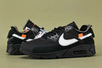 Off-White x Air Max 90 Black - Outsole View on Olive Background Showing Full Black AM90 Rubber Outsole with Square-Block and Wave-Pattern Traction and Orange Square Tab Visible at Tongue