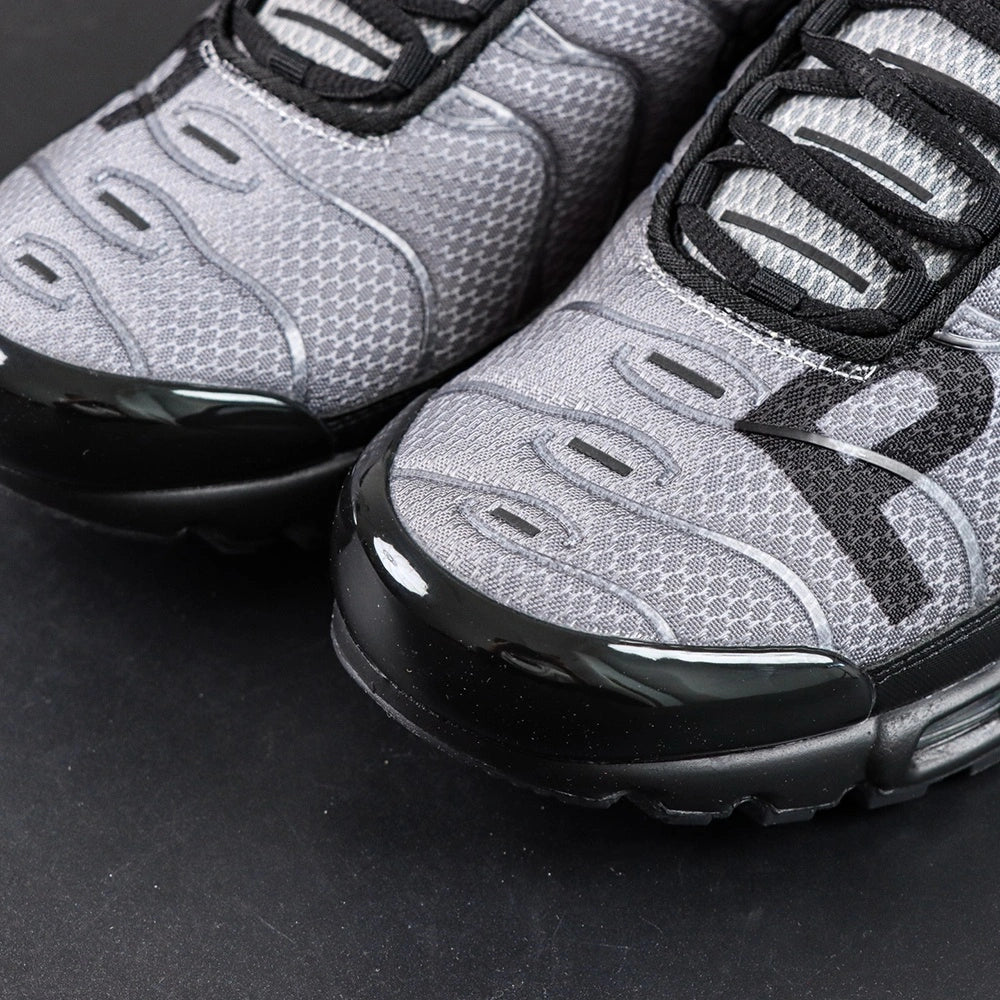 Paris Saint-Germain x Air Max Plus Black Particle Grey - Three-Quarter Top View of Both Shoes on Dark Background Showing Black Patent Leather Wave Dividers Particle Grey Hex Mesh PSG Lettering and Black Rope Laces