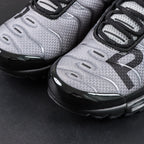 Paris Saint-Germain x Air Max Plus Black Particle Grey - Three-Quarter Top View of Both Shoes on Dark Background Showing Black Patent Leather Wave Dividers Particle Grey Hex Mesh PSG Lettering and Black Rope Laces