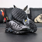 Paris Saint-Germain x Air Max Plus Black Particle Grey - Rear Heel View of Both Shoes on Dark Background Showing Black Patent Leather Heel Counter Yellow Hexagonal Tn AIR Badges and Full Black TN Multi-Tube Air Midsole