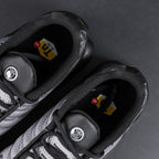 Paris Saint-Germain x Air Max Plus Black Particle Grey - Three-Quarter Lateral View of Both Shoes on Dark Background Showing Full Black and Particle Grey Upper Construction Large PSG Lettering on Hex Mesh and Black TN Midsole