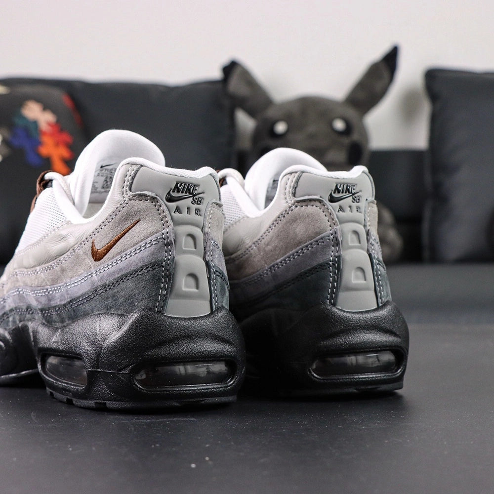 SB x Air Max 95 Cacao Wow 2026 - Rear Heel View of Both Shoes on Dark Background Showing White Grey Gradient Suede Spine Overlays Black Leather Heel Counter NK SB AIR Co-Branding Text and Full Black AM95 Midsole