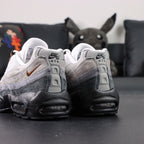 SB x Air Max 95 Cacao Wow 2026 - Rear Heel View of Both Shoes on Dark Background Showing White Grey Gradient Suede Spine Overlays Black Leather Heel Counter NK SB AIR Co-Branding Text and Full Black AM95 Midsole