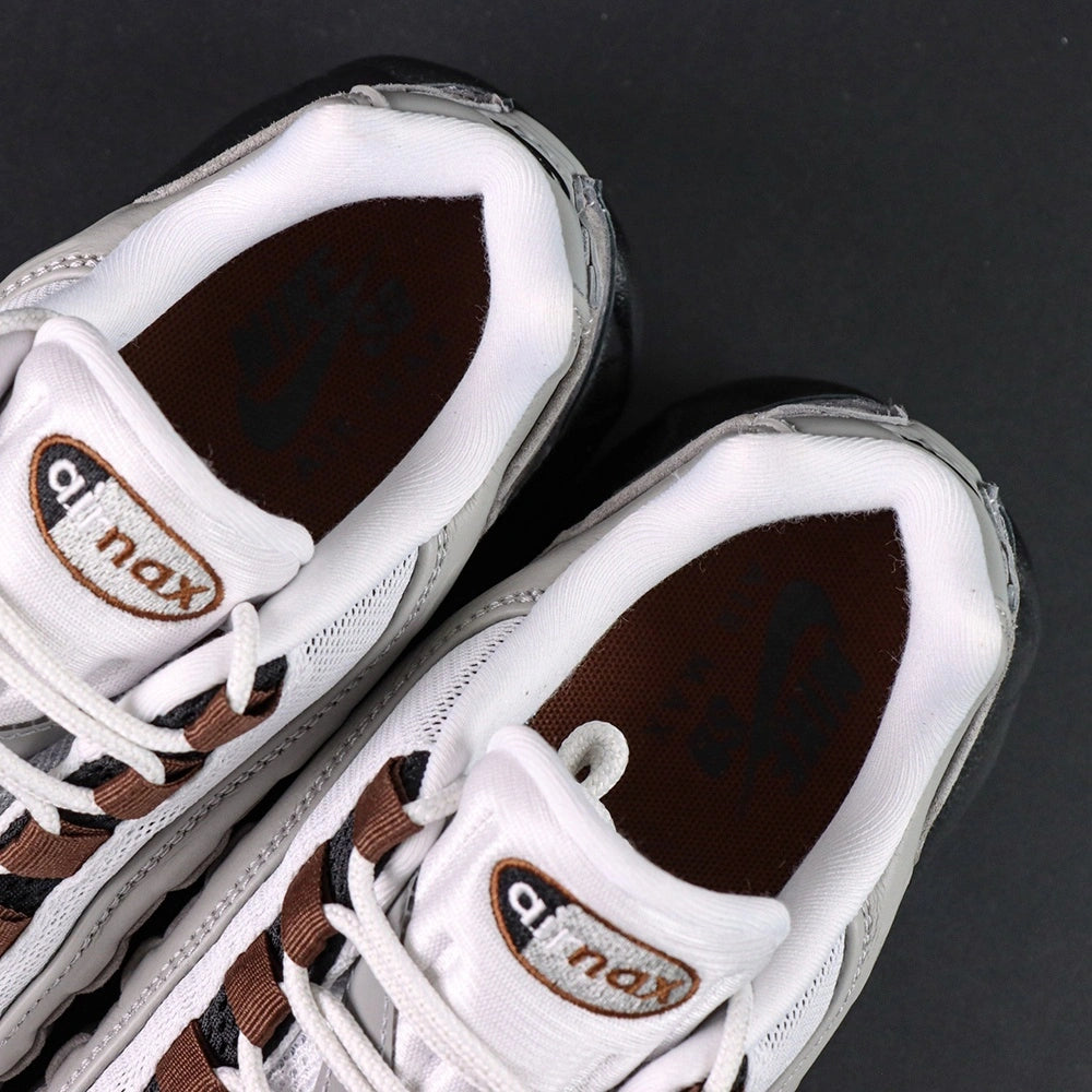 SB x Air Max 95 Cacao Wow 2026 - Three-Quarter Lateral View on Dark Background Showing Full White Grey Black Gradient AM95 Upper Cacao Wow Brown Grosgrain Ribbon Lace Tabs and Brown Mini Swoosh