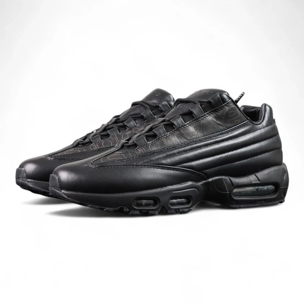 Supreme x Air Max 95 Lux Black - Three-Quarter Lateral Top View of Both Shoes on Dark Background Showing Full Premium Black Leather AM95 Upper Tone-on-Tone Debossed Supreme New York Cursive Script and Black Metal Ball-Chain Dubrae