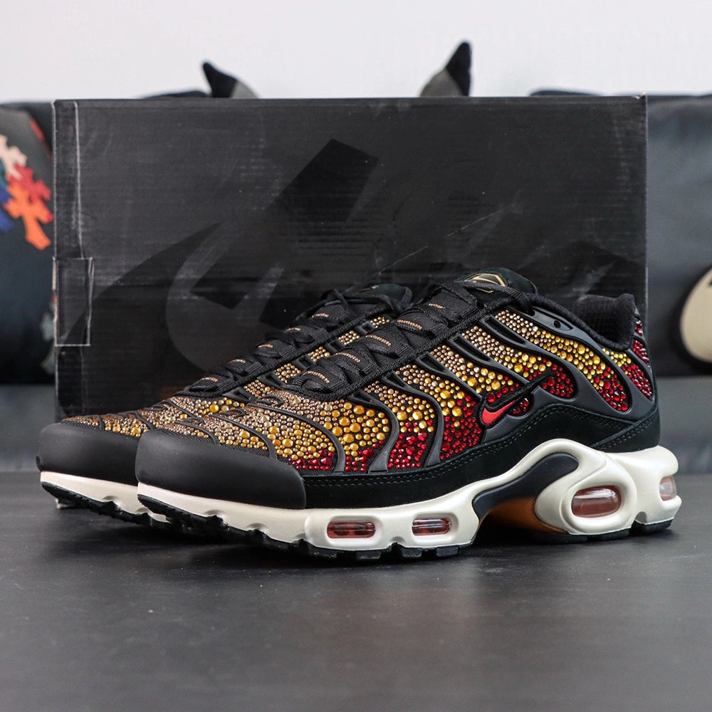 Swarovski x Air Max Plus Sunset - Three-Quarter Lateral View with Pikachu Plush on Dark Background Showing Swarovski Crimson to Gold Crystal Gradient Across TN Wave-Form Panels Red Swoosh and White Midsole with Amber-Tinted TN Air Units