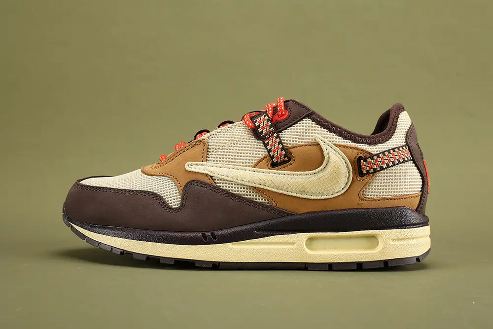 Air Max 1 Cactus Jack Baroque Brown Wheat Cream University Red - Toe Box Close Up on Olive Background Showing Baroque Brown Smooth Nubuck Toe Box Overlay with Tonal Edge Stitching Cream Coarse Square-Grid Woven Mesh Toe Box Body Baroque Brown Suede Mudguard and Cream Aged AM1 Midsole with Dark Navy Rubber Outsole and Lug Traction