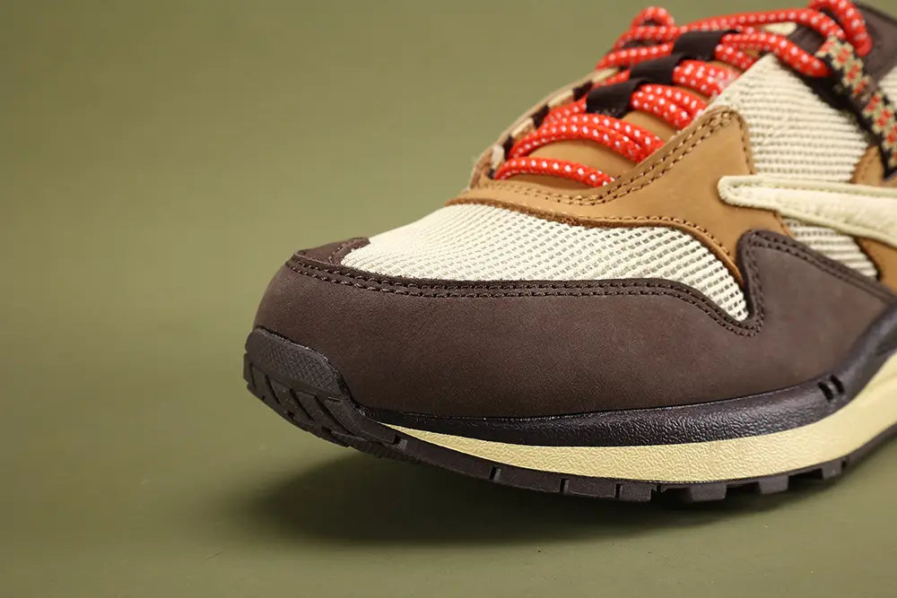 Air Max 1 Cactus Jack Baroque Brown Wheat Cream University Red - Rear View of Both Shoes on Olive Background Showing University Red Triangular Pennant Flag Patches at Heel Counter with Co-Branded Text and Swoosh in White on Left and CACTUS JACK Text in Cream on Right Black Multicolour Woven Webbing Heel Pull Tabs Cream Corduroy Collar University Red Collar Lining and Cream Aged AM1 Midsole